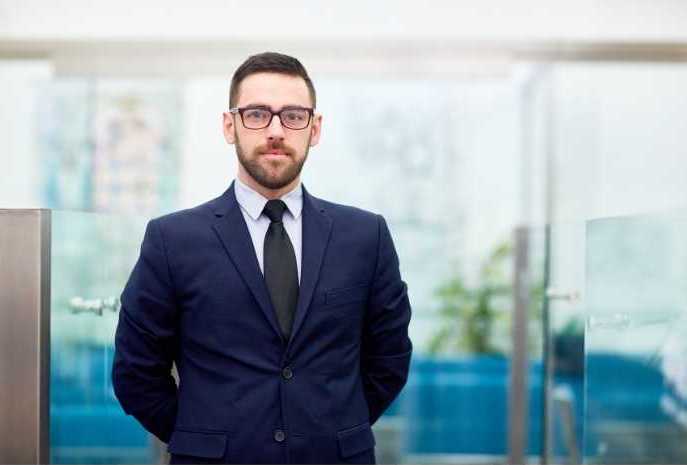 A professional in a suit and tie standing confidently in a well-lit office space.